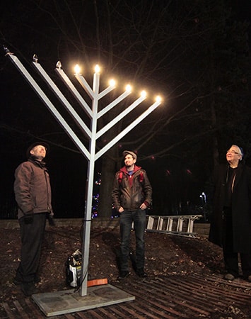 Gary Bercovitch, president of the Beach Hebrew Institute, right, smiles as a menorah shared by Chabad-Lubovitch of Danforth-Beaches is lit at Kew Gardens on Dec. 20. After about 30 years, Bercovitch said his congregation was surprised to find their own menorah couldn't be used because it didn't meet the electrical safety requirements. PHOTO: Andrew Hudson