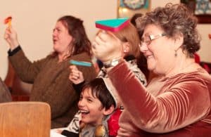 Six year-old Arik laughs as his grandmother Ruth Blanch, right, joins in spinning noisy ‘graggers’ every time someone reading Esther’s story says the name ‘Haman.’ PHOTO: Andrew Hudson