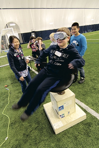 Phoebe Yung, a Grade 11 student at Monarch Park Collegiate, takes students from Westwood Middle School for a spin in a chair modelled on astronaut training exercises. Spinning upsets the vistibular system – three fluid-filled canals in the inner ear that give people a sense of balance. PHOTO: Andrew Hudson